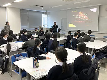 椅子に座って男性研究者の話を聞く生徒達