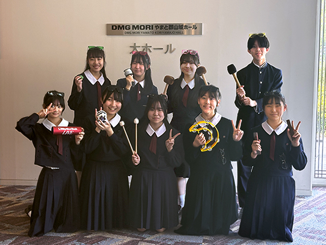 大ホールの前で楽器の小道具持ってポーズする女子8人と男子1名