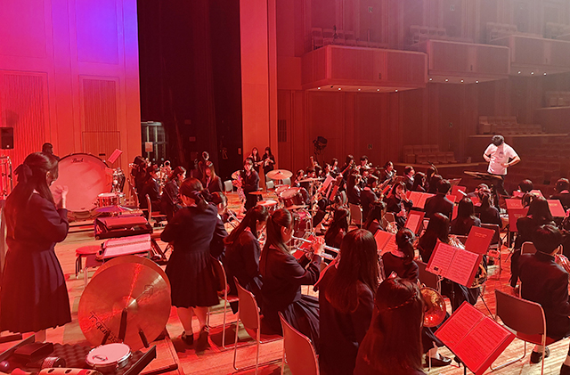 ホールの舞台で赤い照明中演奏練習中の生徒達