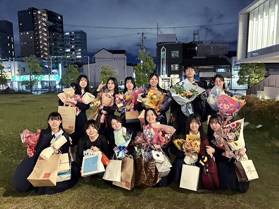 野外で花束を持って笑顔で記念撮影する高校3年生11名と教員
