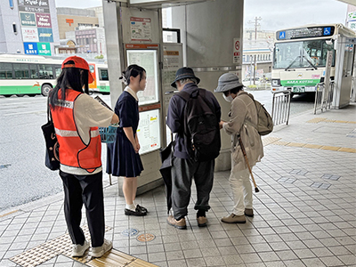 ご高齢の男性と女性に説明する女子生徒1人と補導員1人