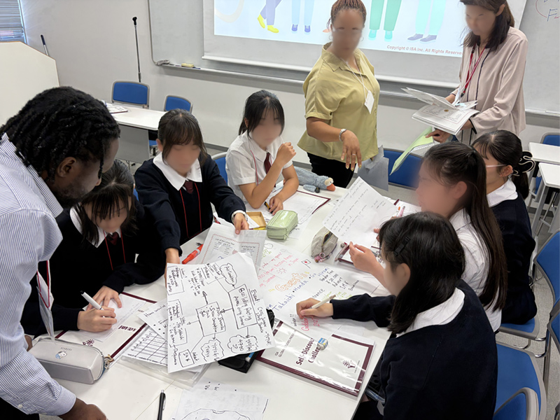 3人の教員と6人の女子生徒がプリントをまとめている