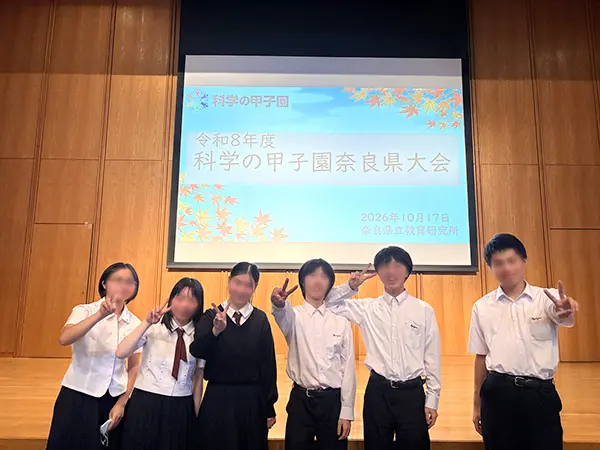 会場のプロジェクタの前で生徒6人ピースして記念写真