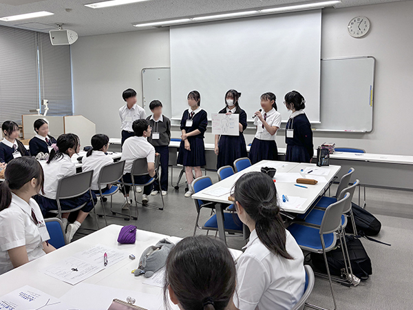6人の生徒が立って発表しているのを聞いている他の生徒達